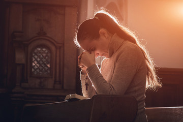 Christian woman praying in church. Hands crossed and Holy Bible on wooden desk.