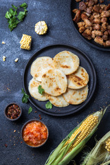 COLOMBIAN FOOD. Maize AREPAS and fried pork chicharron ans colombian tomato sauce. Top view. Black background