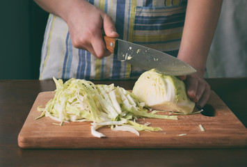 Woman cook sauerkraut or salad on wooden background. Step 1 - Chop Cabbage. Fermented preserved...