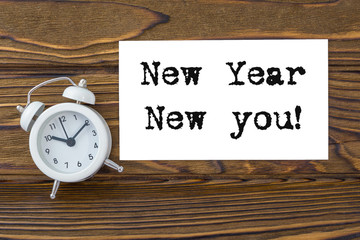 new year new you! text on business card, clock alarm, on wood background texture. business concept