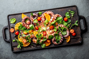 Whole octopus salad with orange, tomatoes and cress salad served on board with wine © lblinova