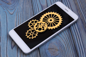 phone and gears on the screen, on a background of a wooden texture background. Digital composition, repair or application updates, smartphone