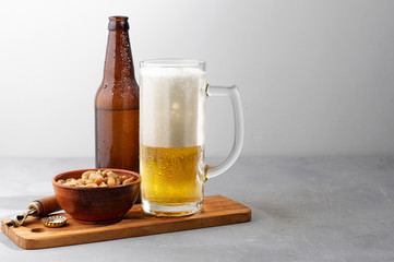 Lager beer pouring in glass and bottle with salted peanuts on gray concrete background