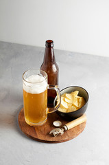 Lager beer in glass and bottle with potato chips on gray concrete background