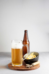 Lager beer in glass and bottle with potato chips on gray concrete background