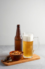Lager beer pouring in glass and bottle with salted peanuts on gray concrete background