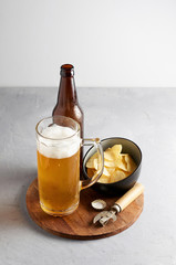 Lager beer in glass and bottle with potato chips on gray concrete background