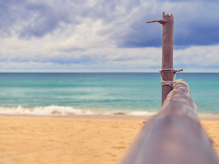 The wooden crossbar is located on a tropical beach. In the distance you can see the sea or the ocean and the sky with clouds.