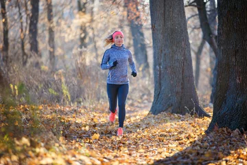 Fotobehang Jonge vrouw joggen op pad in herfst park © skumer