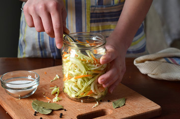 Woman cook sauerkraut or salad on wooden background. Step 5 - Put the cabbage in the jars. Fermented preserved vegetables food concept.