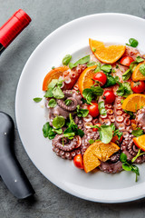 Whole octopus salad with orange, tomatoes and cress salad on white plate. Top view