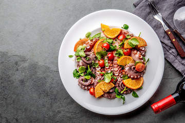Whole octopus salad with orange, tomatoes and cress salad on white plate. Top view