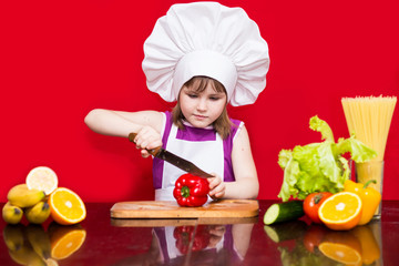 Happy little girl in chef uniform cuts vegetables in kitchen. Kid chef. Vegetarian. Cooking Concept