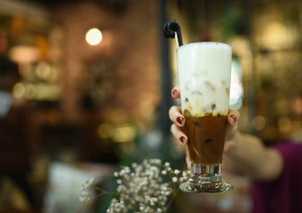 Ice coconut coffee in woman hand at coffee shop. A cup of layer coffee and milk holding by a girl with red color nails. Vintage coffee shop. Testy mocha coffee with milk.