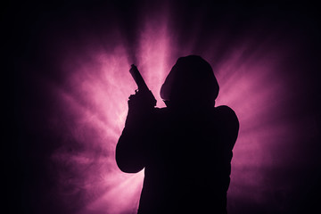 Silhouette of man with assault rifle ready to attack on dark toned foggy background or dangerous...