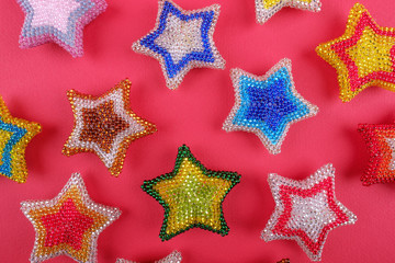Fototapeta na wymiar Christmas New Year star stars different colors made from beads handmade on red pink background