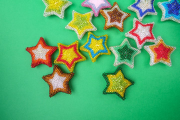 Fototapeta na wymiar Christmas New Yearstar stars different colors made from beads handmade on green background