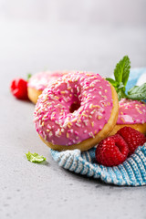 Pink raspberry donuts on gray concrete background with mint. Birthday party food concept with copy space.