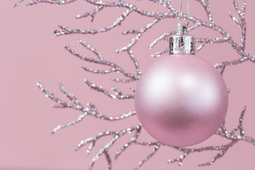 Shiny silver branch with pink Christmas bauble monochrome on pink background