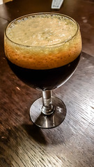 A glass of dark beer stands on a wooden table