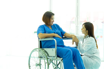 Obraz premium Mature obstetrician gynecologist riding pregnant woman on wheelchair at maternity hospital. Health care and empathy concept.