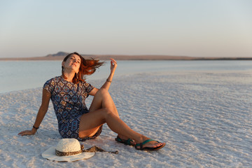 Fototapeta na wymiar Calm girl enjoying sun, sits on the ground covered with salt close to lake