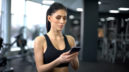 Fototapeta premium Purposeful lady in sportswear scrolling smartphone application, motivation