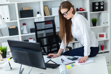 A young girl sat down on the table and works with a computer, documents and calculator