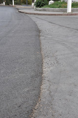 Partly repaired roadway with a vertical edge between the newly laid asphalt concrete on the left and the older area on the right.