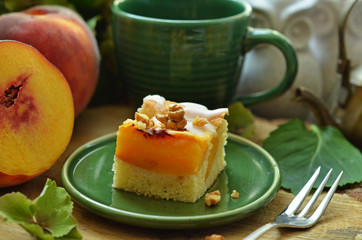 A piece of cake with peaches on a green plate. Peaches and green cup in the background