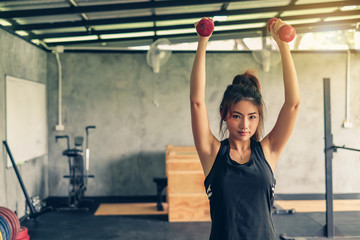 Beautiful young asian woman lifting dumbbell at gym