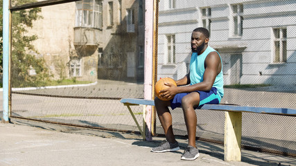 Melancholic Afro-American male sitting on bench and playing ball, loneliness