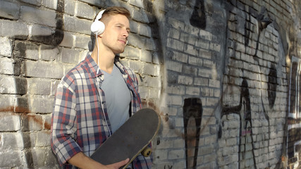 Fototapeta na wymiar Handsome male with skateboard listening favorite music on smartphone, hobby