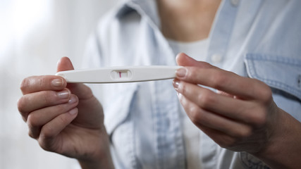 Female holding negative pregnancy test in hands, demonstrating before camera
