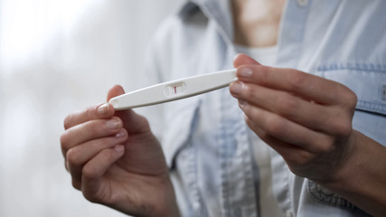 Female hands holding negative pregnancy test and showing it into camera, closeup