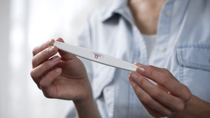 Female holding positive pregnancy test in hands, demonstrating it before camera