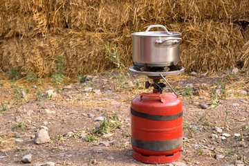 Small propane gas cylinder and heating pad for cooking. Cooking in a pan in field conditions.