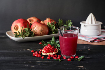 Freshly squeezed pomegranate juice in a glass near ingredients on black wooden background, healthy drinks concept.