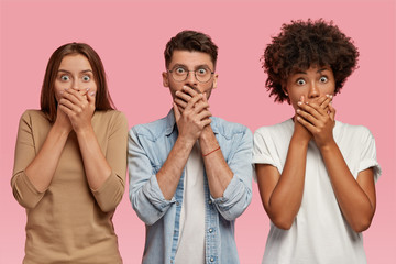 Stupefied emotive mixed race colleagues cover mouthes, hear bad news from employer, stare at...