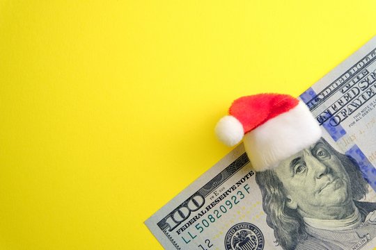 In the New Year without financial debt. Red Santa Claus hat on Franklin's head on one hundred dollars. Yellow background with copy space. How much money do people spend on winter holidays