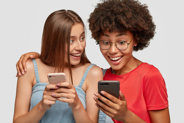 Multiracial friends embrace and share multimedia files via cell phone bluetooth, enjoy wireless...