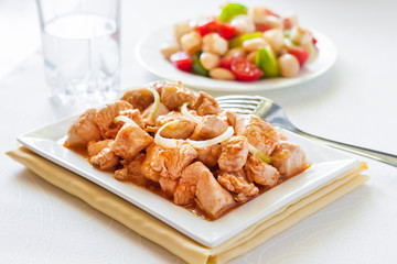 Turkey stew in tomato mustard sauce with onion on square plate