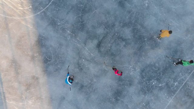 Children playing hockey ice field, aerial video. Ice hockey sport young boys players outdoors. Drone flying over ice hockey players kids. 