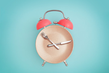 Alarm clock and plate with cutlery . Concept of intermittent fasting, lunchtime, diet and weight...
