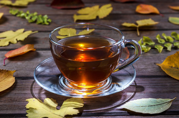 Glass cup of tea on a wooden table with yellow leaves.