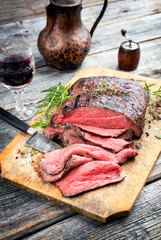 Traditional barbecue dry aged sliced roast beef steak with herbs as closeup on an old cutting board