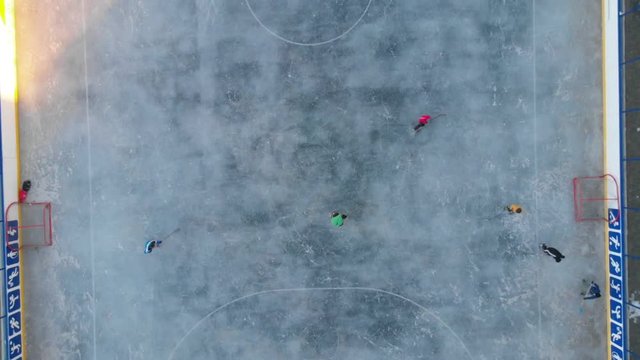 Children playing hockey ice field, aerial video. Ice hockey sport young boys players outdoors. Drone flying over ice hockey players kids. 