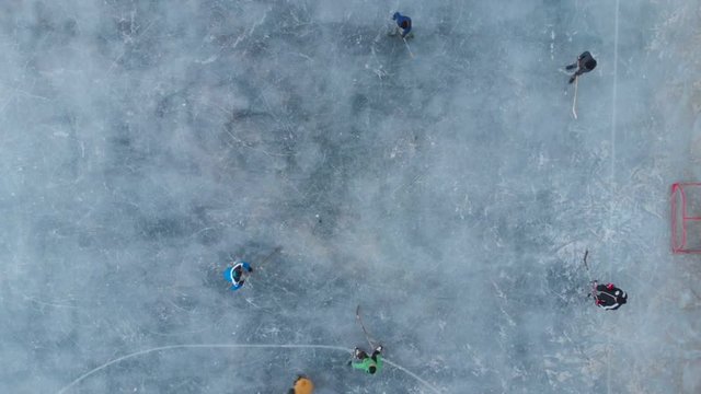 Children skating playing hockey outdoor stadium aerial view from above. Winter sports kids playing hockey drone shot. 