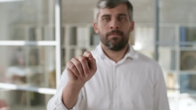 Medium shot of serious businessman with beard tapping and swiping data on invisible augmented reality screen in office. Footage suitable for adding AR elements