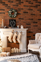 Loft apartments, brick wall with candles and Christmas tree wreath. White wool socks for Santa on the fireplace. Knitted carpet and chair, Christmas tree